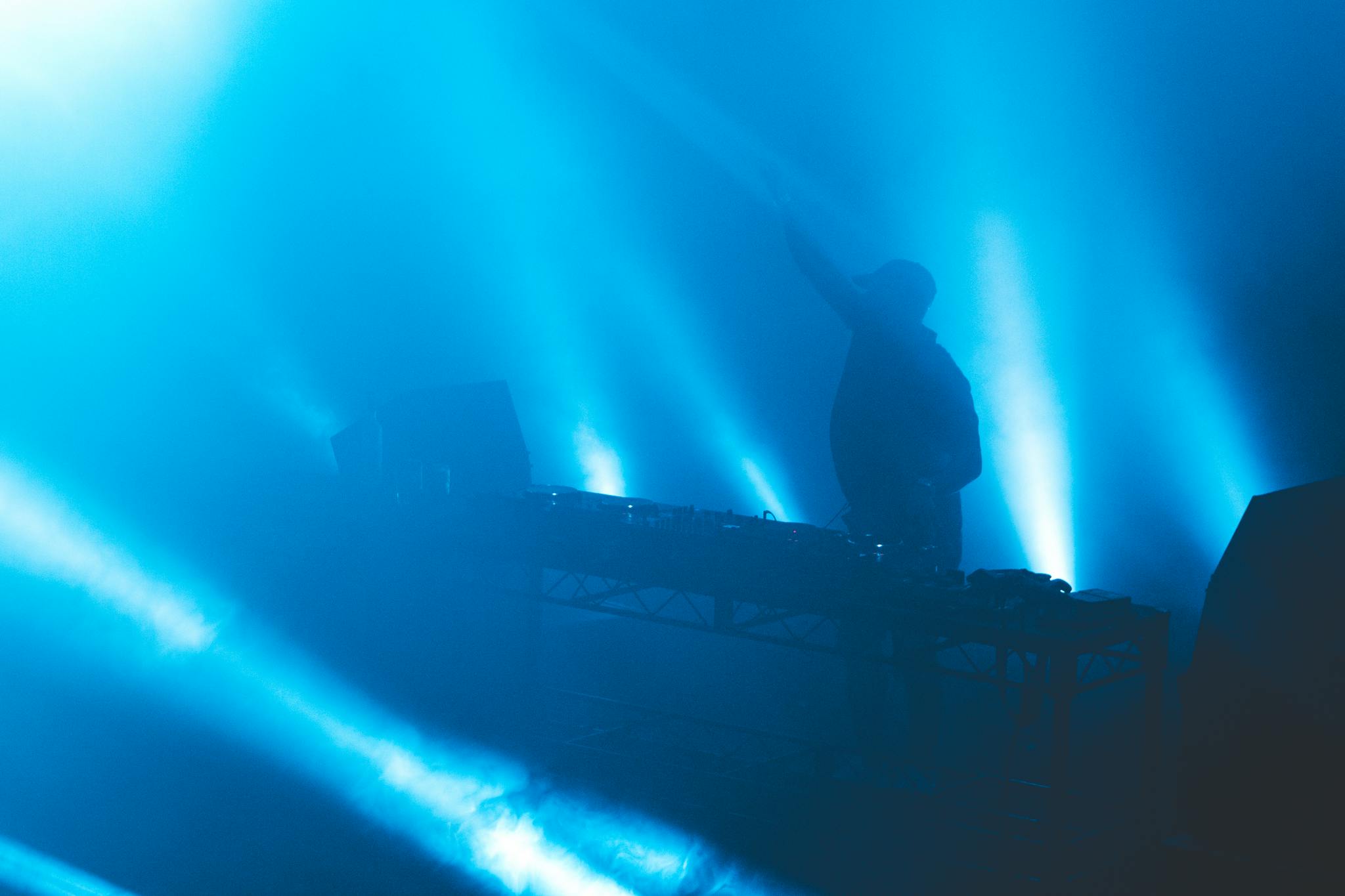 A DJ performs amidst vibrant blue lights at an energetic nightclub event.