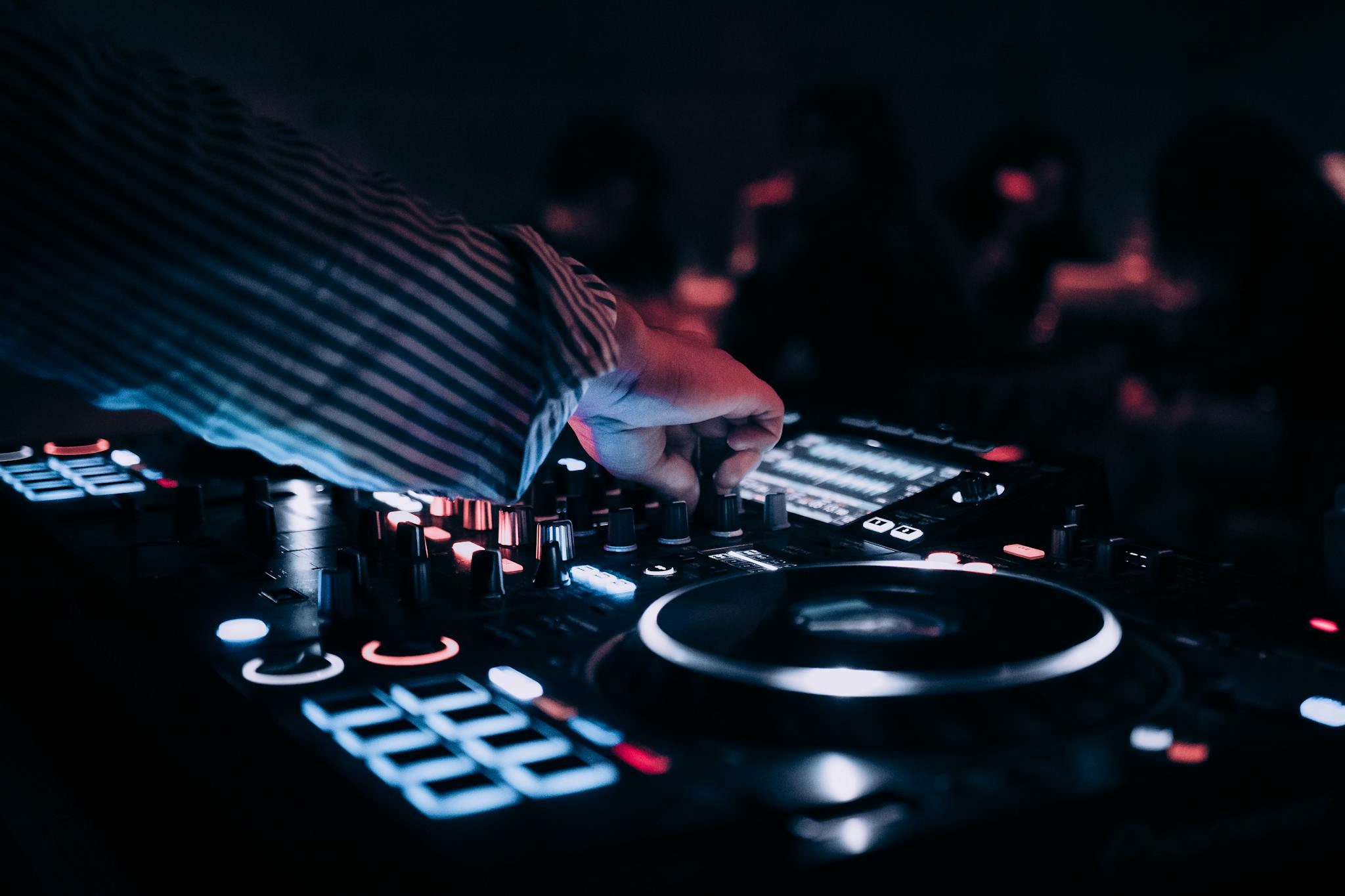 Close-up of DJ mixing music on an illuminated console at a nightclub.