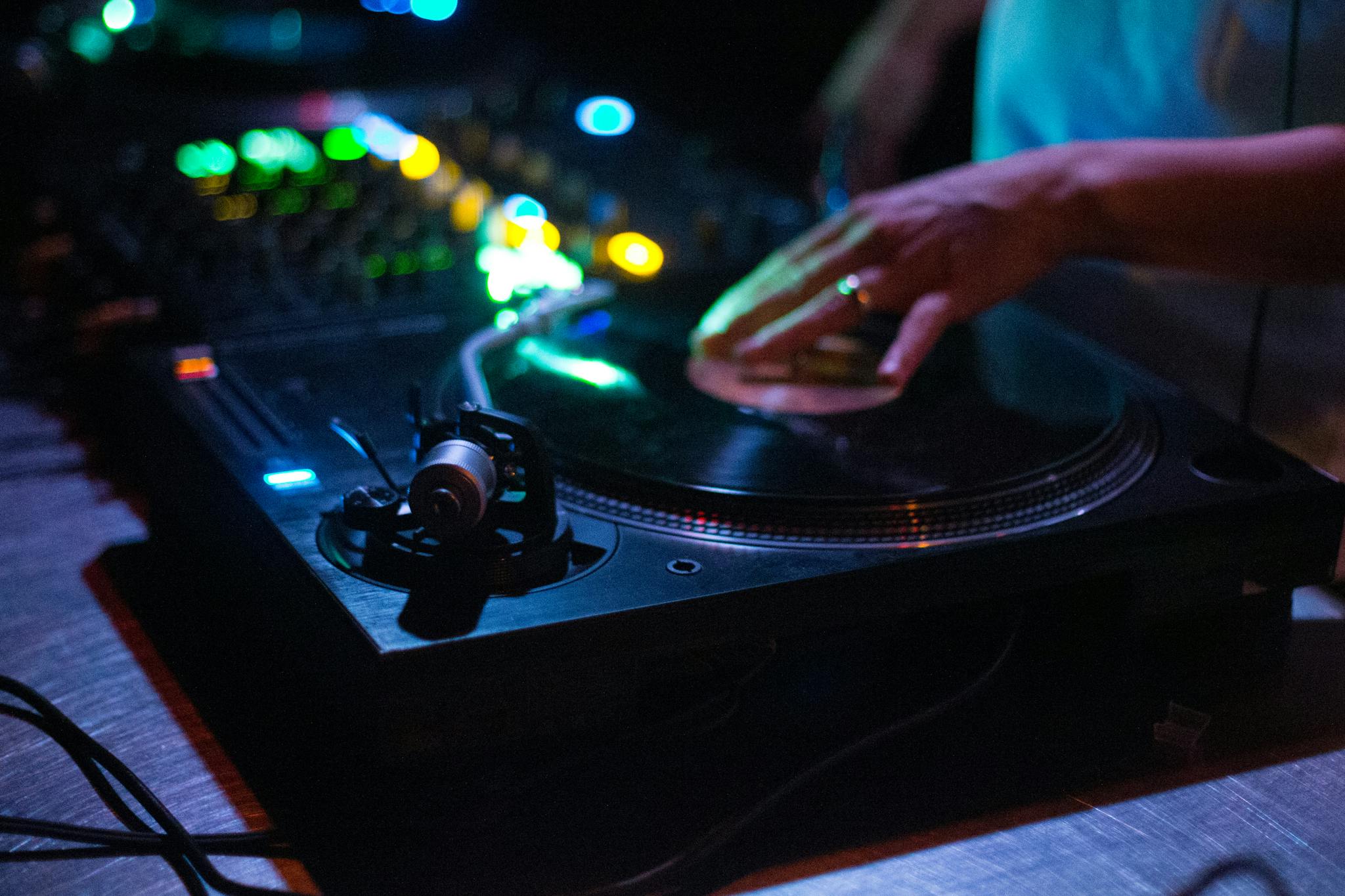 Close-up of DJ mixing on a turntable with colorful club lights, capturing vibrant nightlife atmosphere.
